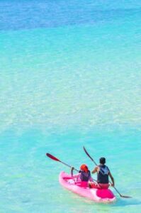Two people kayaking on a turquoise ocean, enjoying a sunny day outdoors.