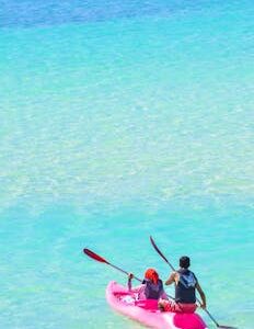 Two people kayaking on a turquoise ocean, enjoying a sunny day outdoors.