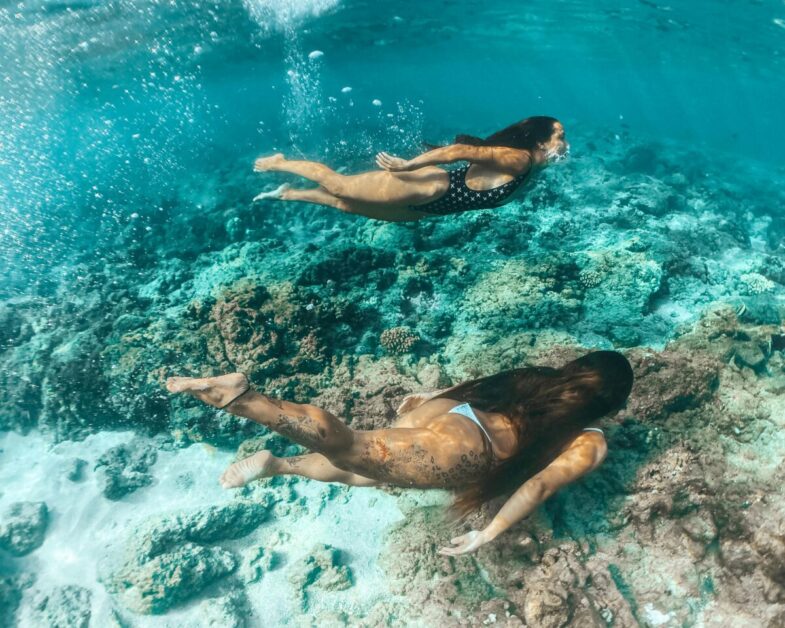 Two women freediving in a vibrant coral reef underwater, showcasing oceanic beauty.