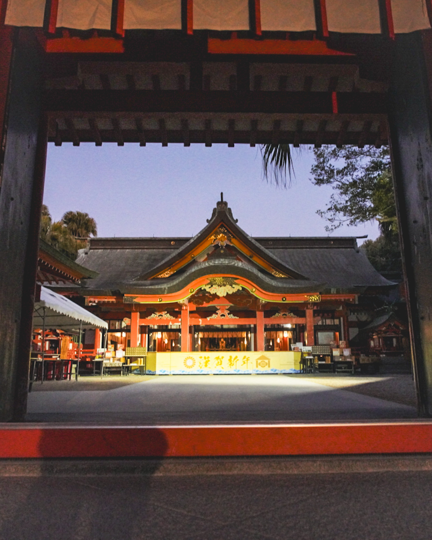 Aoshima, Udo Shrine, Sun Messe Nichinan & Obi Castle Private Tour 1 Through Aoshima shrine gate, warm orange-lit lanterns glow at Aoshima Shrine in Miyazaki during evening light, creating a serene temple scene.